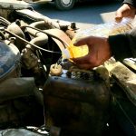 a man is filling a bottle of liquid into a car's engine
